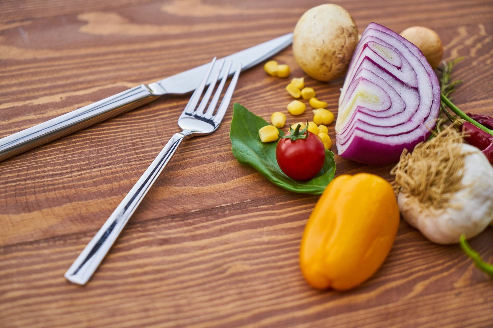 Fresh vegetables laid out on a wooden table: onion, pepper, tomato and garlic